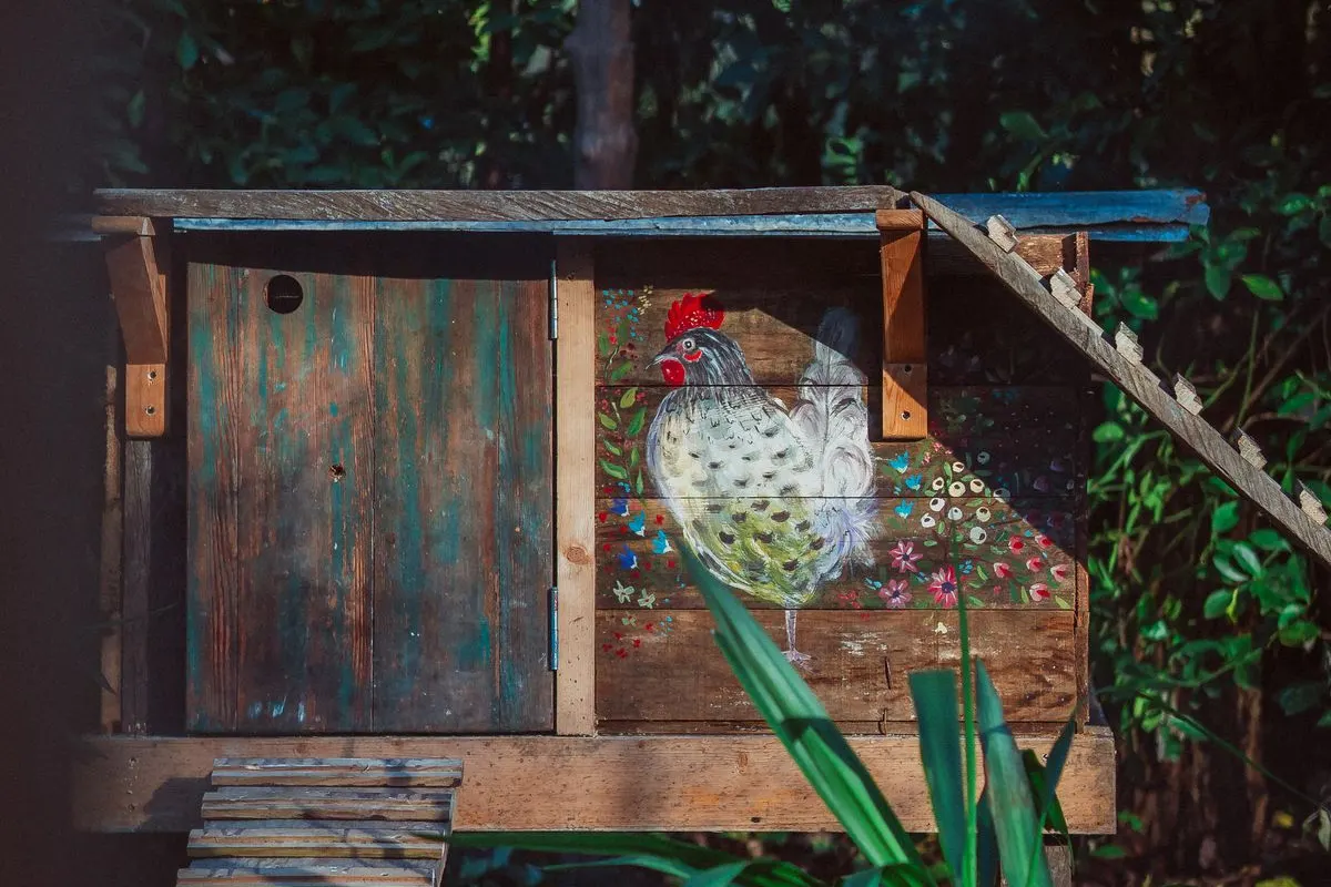 A small wooden backyard coop with a hen painted on its side, set among trees